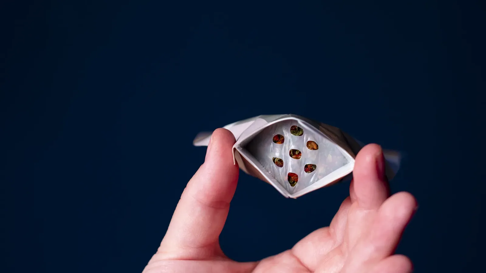 Hånd som holder en åpnet Push&Dose-topp med membranen synlig